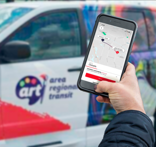 Image of person using app to book an ART On-Demand ride with ART On-Demand vehicle in background