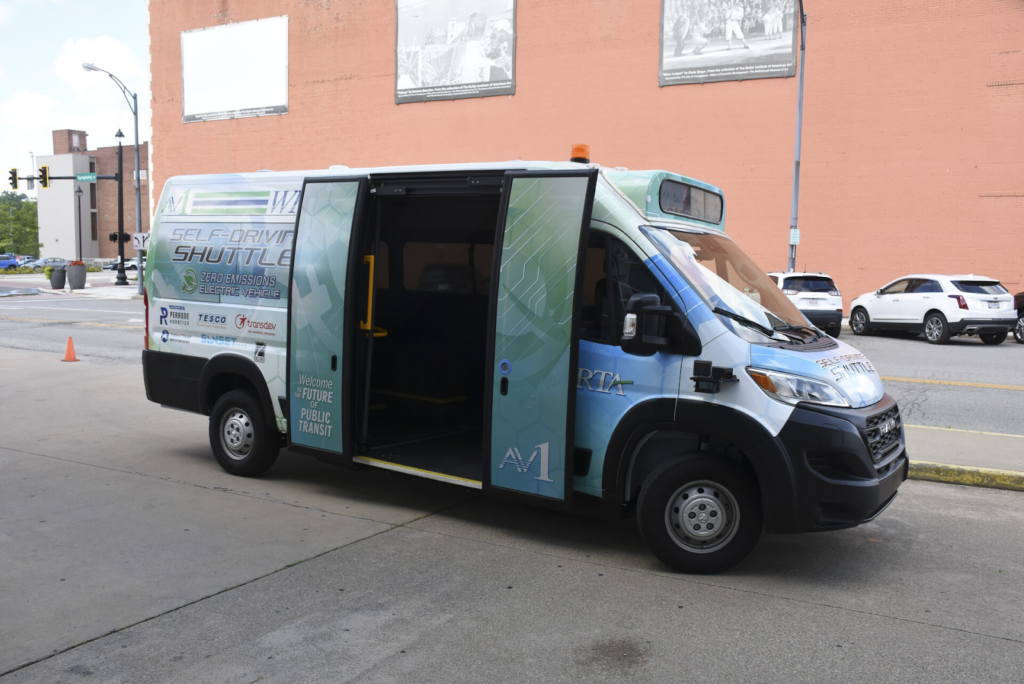 A side view of an AV1 vehicle is parked alongside a curb with its passenger doors open.