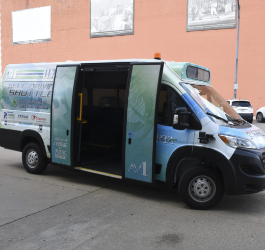 A side view of an AV1 vehicle is parked alongside a curb with its passenger doors open.