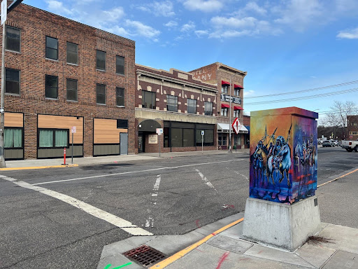 A painted electrical box in the foreground, an empty street and brick buildings in the background