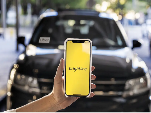 Image of person using Brightline app on smartphone in front of an Uber vehicle