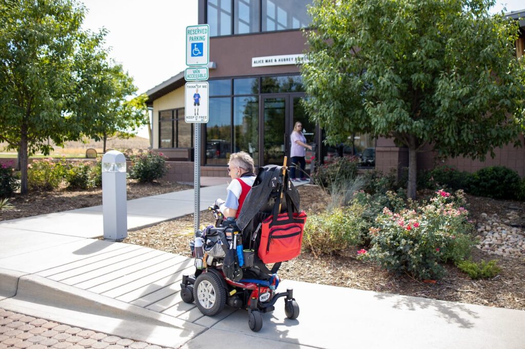 Woman in powerchair using curb cut that is marked with handicapped sign and truncated domes