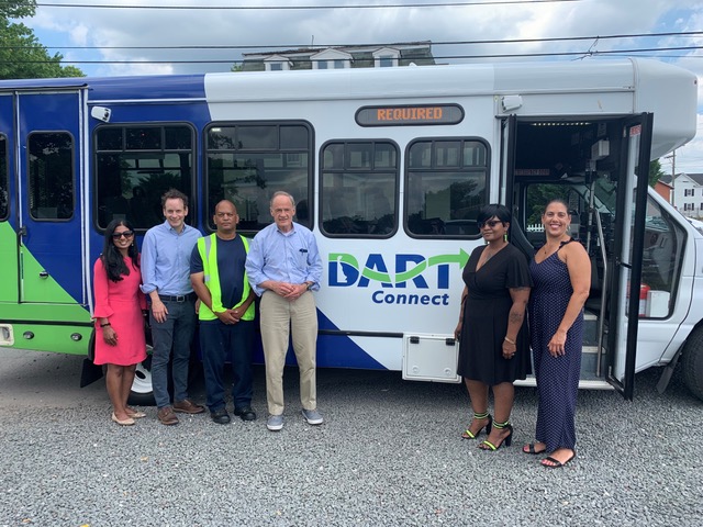 Six people stand in front of a DART Connect cutaway bus