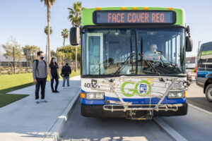 Passengers with masks waiting to board a bus. 