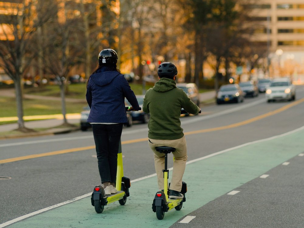 Two people wearing helmets and riding scooters.