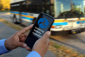 Someone holds a phone with the FTA logo and the words enhancing mobility innovation on it, in front of a bus