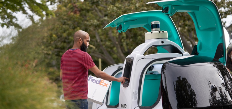 Image of person holding a FedEx package at a Nuro vehicle