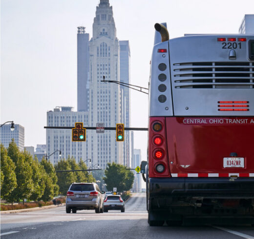 A red and white bus in the foreground with a stoplight and skyscraper in the background