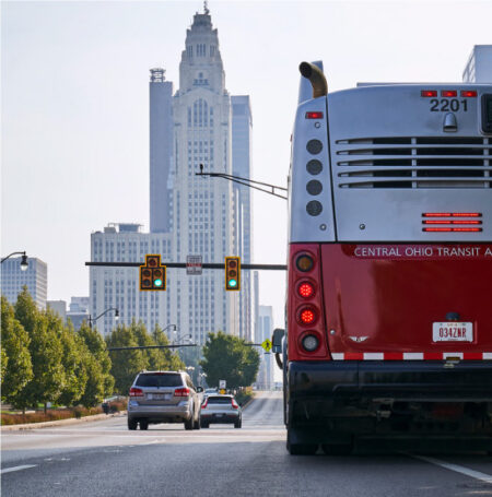 A red and white bus in the foreground with a stoplight and skyscraper in the background