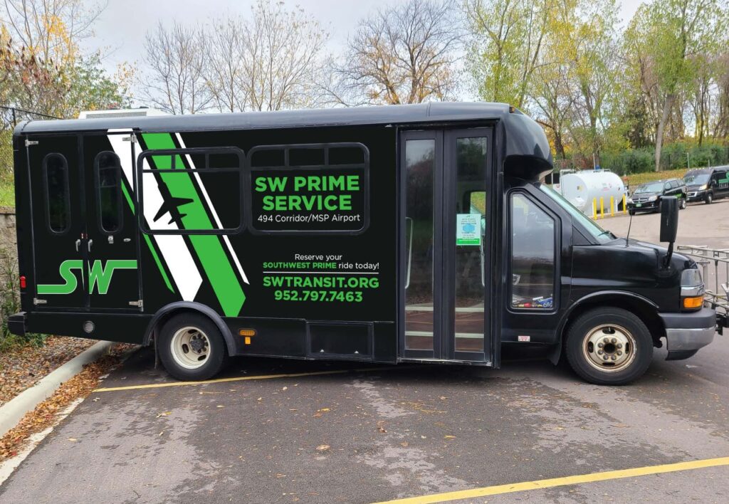 A twelve-passenger van with SW Transit branding drives down a street.