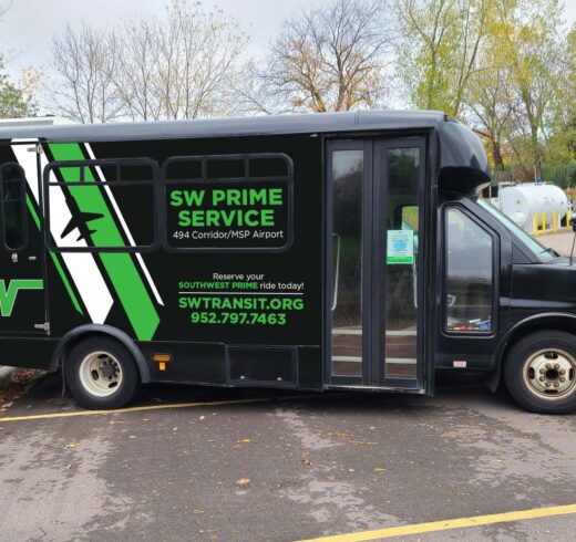 A twelve-passenger van with SW Transit branding drives down a street.