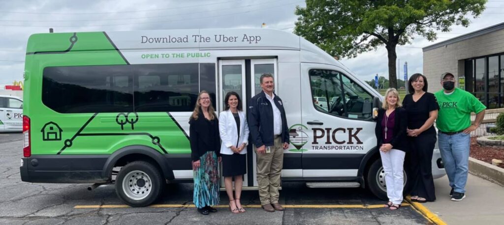 A group of people smile in front of a microtransit vehicle.