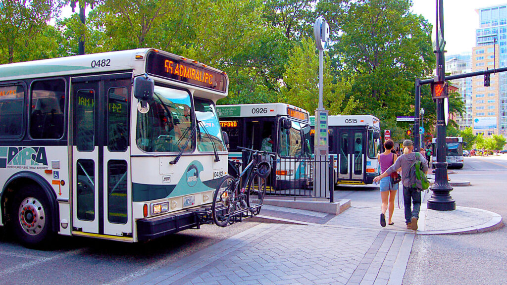 Image of couple walking in front of RIPTA buses during a red light