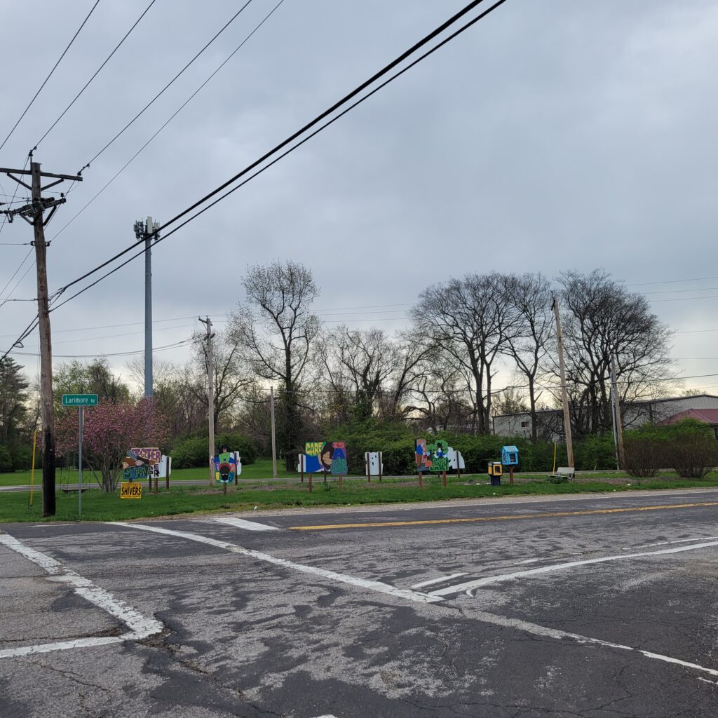 a road in the foreground and several small freestanding murals in the grass on the other side