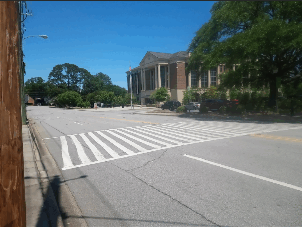 A road in the foreground with a painted crosswalk and a building in the background