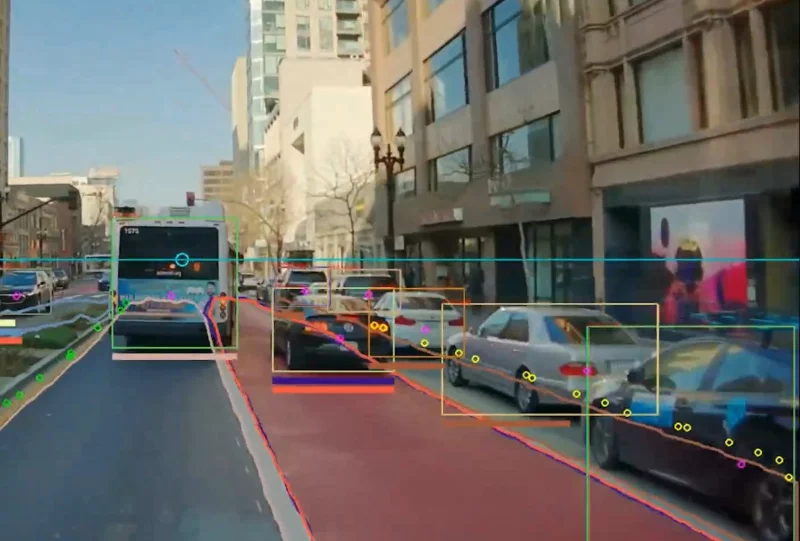 A camera’s view of a dedicated bus lane with a car illegally parked, detected by AI software. The camera’s screen includes a variety of rectangles and other shapes fixed on vehicles, with colors corresponding to the software’s identification of a bus, parked car, illegally parked car, etc.