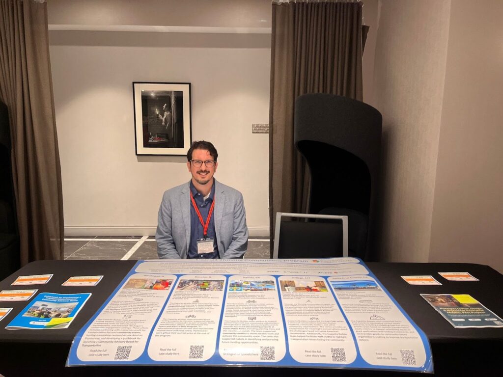 a man sits behind a table with a poster in front of him