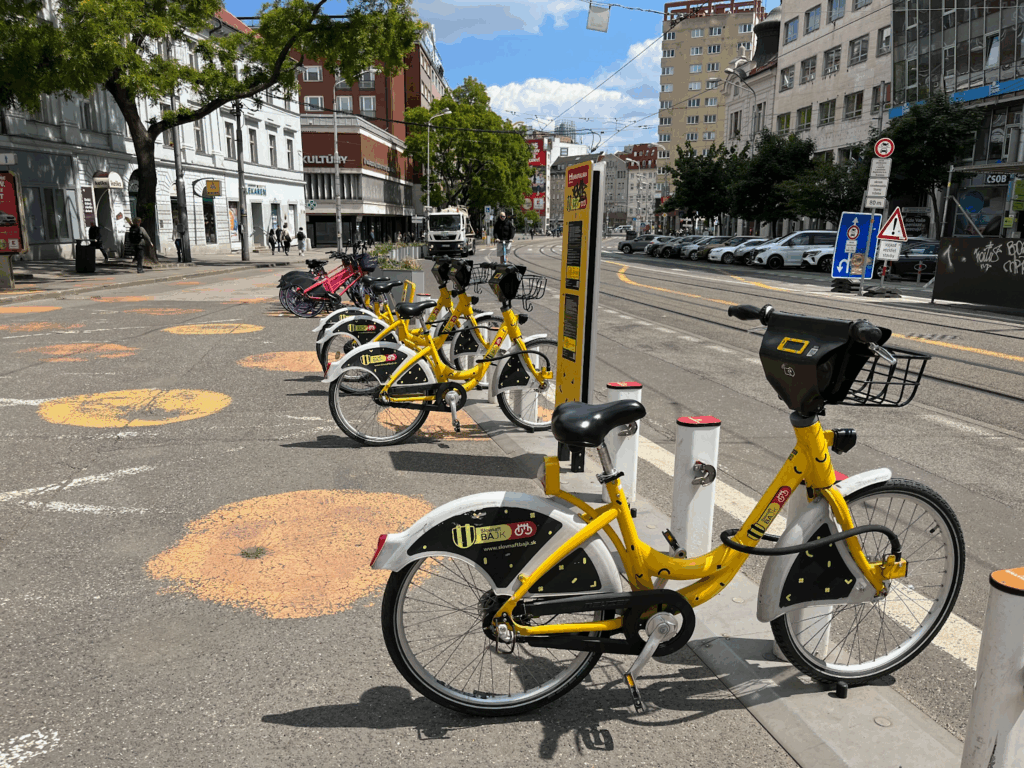 Several yellow bikeshare bikes docked at a docking station next to a road