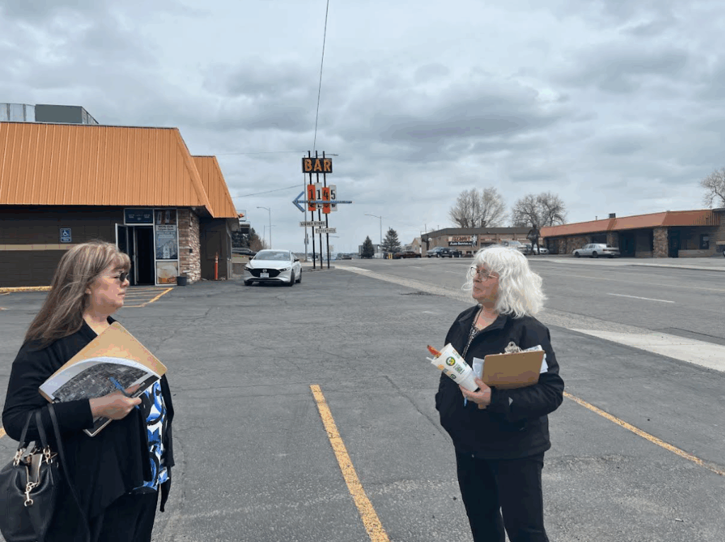 Two women stand outside in a parking lot facing each other