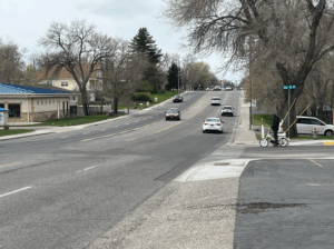 a street with several cars and a bicyclists waiting to cross