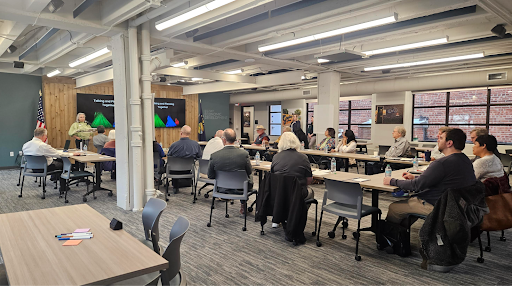 A group of people sit around tables watching a presentation