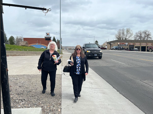 Two women walk along a sidewalk facing the camera
