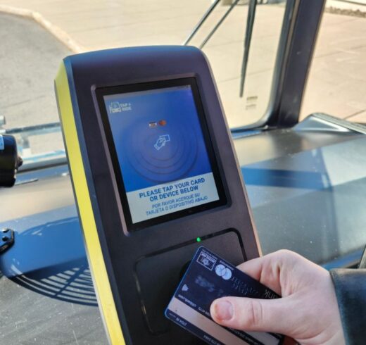 a hand taps a credit card to a contactless reader on a bus