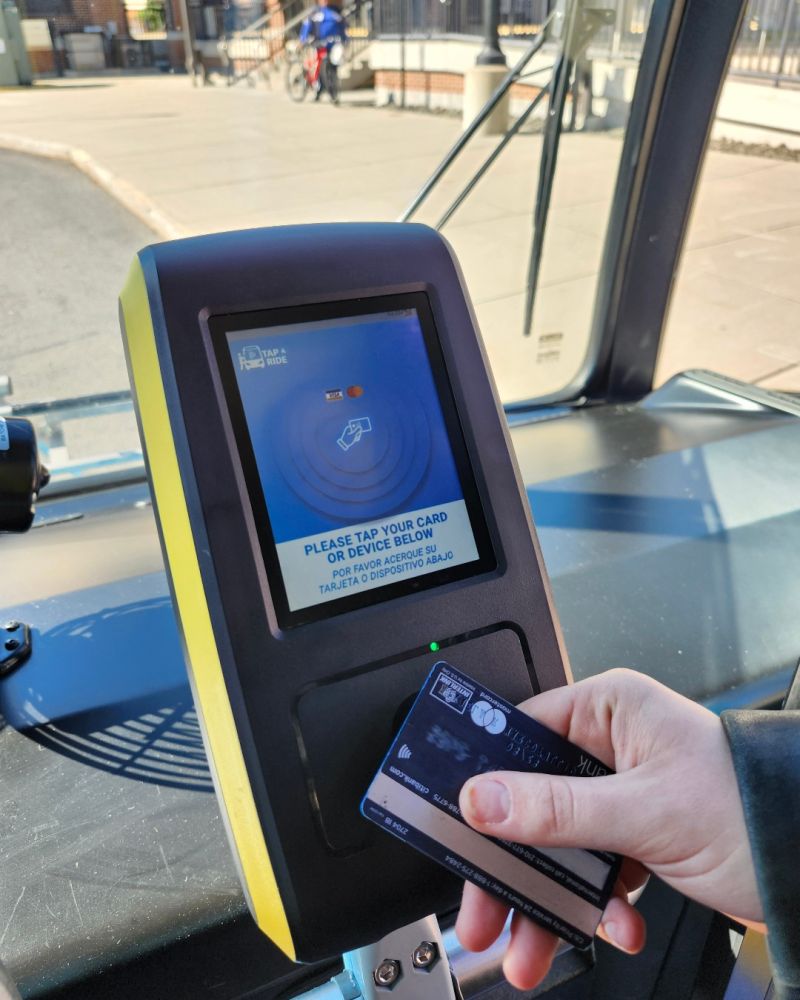 a hand taps a credit card to a contactless reader on a bus
