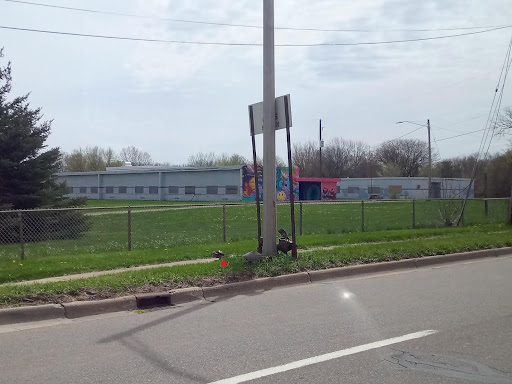 A building in the background with a road, grass, and fence in the foreground