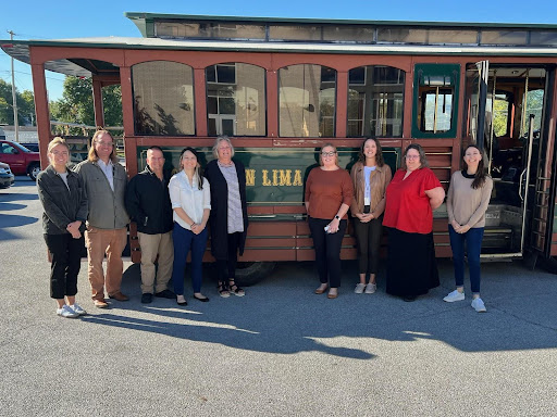 Nine people stand in front of a trolley with "Lima" written on the side