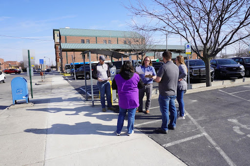 five people stand on the sidewalk talking to each other
