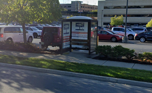 An empty bus shelter on a sidewalk. There is grass between the sidewalk and the road