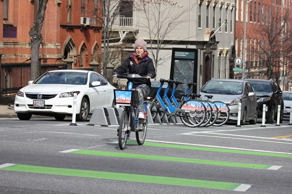 A woman rides a bikeshare bike with a white car in the background