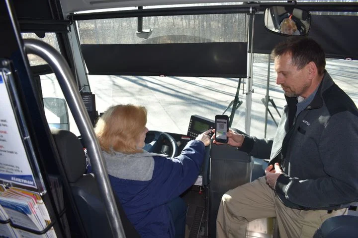 a man boards a bus and shows the bus driver a qr code on a phone screen