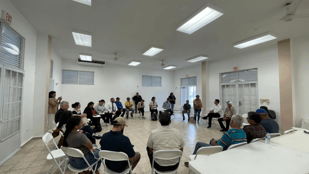 many people sit in a white room in a large circle facing each other